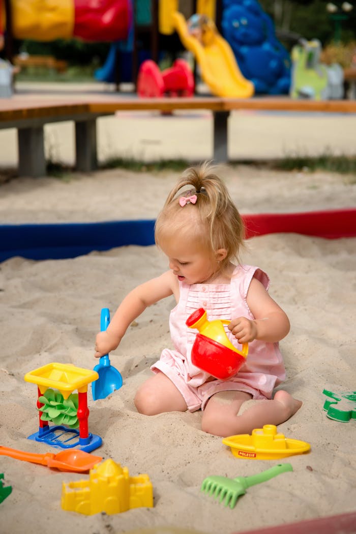 A young girl plays in a sandbox with colorful toys, enjoying a sunny outdoor day.