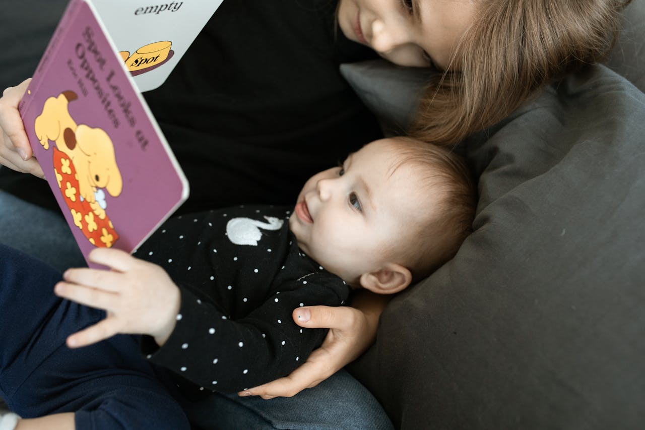 A touching scene of a big sister reading to her baby sibling on a cozy sofa.